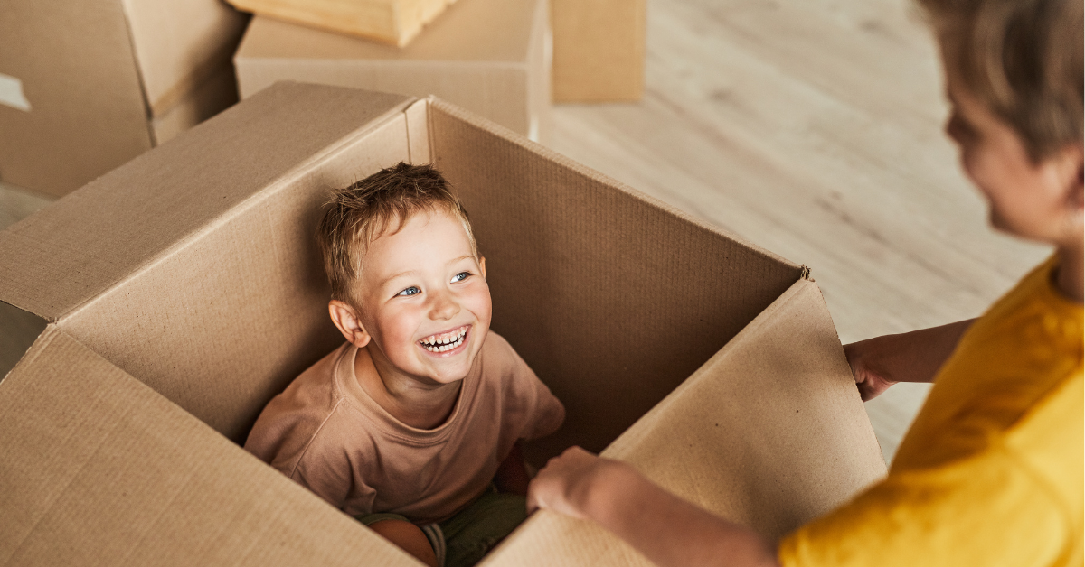 A smiling toddler inside of a moving box, playing with his mother