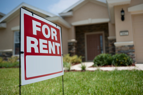 A for rent signage with a beige home in the background