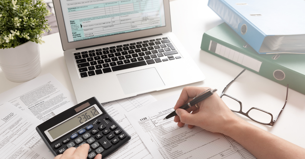 Person with a calculator and some paperwork with a laptop as a background