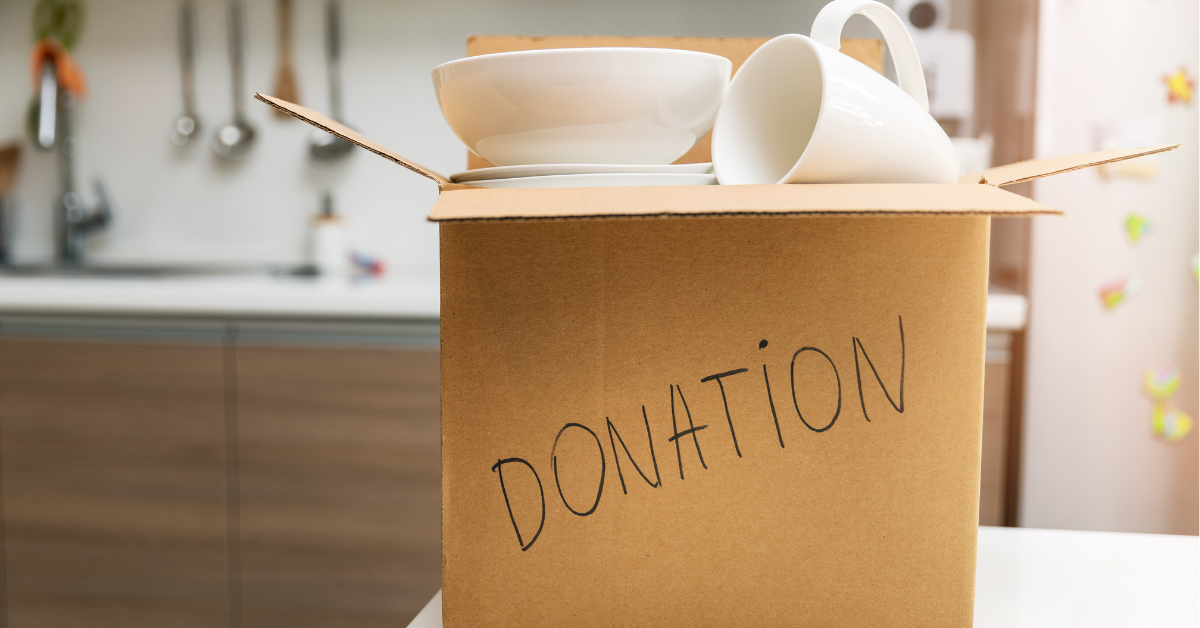 Cardboard box labeled ‘DONATION’ filled with white kitchenware items, placed on a kitchen counter