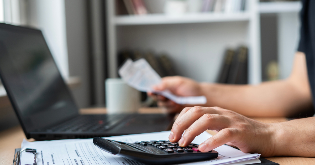 Person with a calculator and some paperwork with a laptop as a background