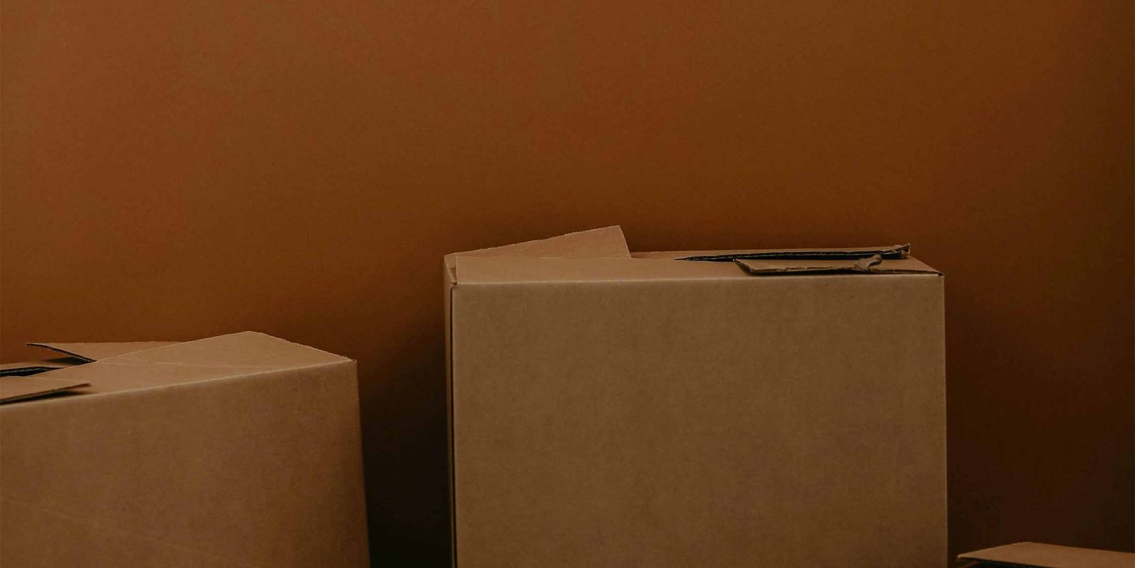 Cardboard moving boxes against a brown wall.