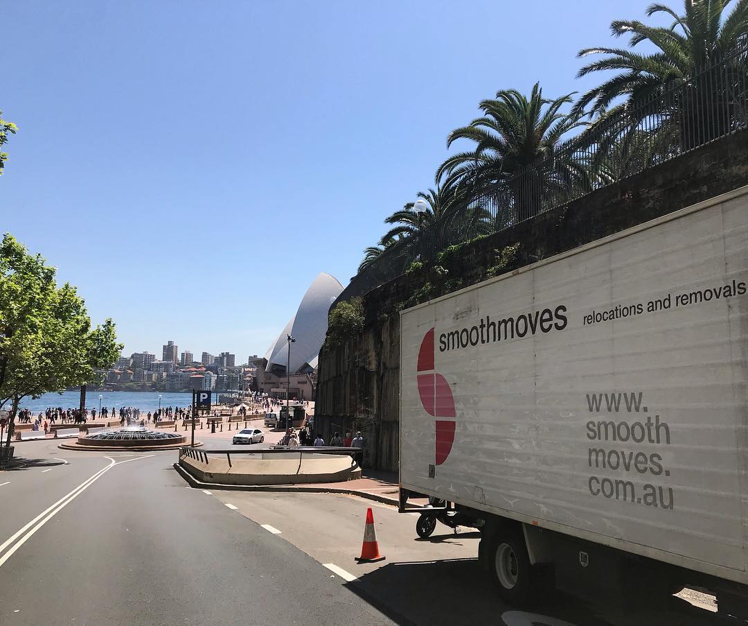 A Smooth Moves removal truck is parked on a street near the waterfront, with the iconic Sydney Opera House and city skyline visible in the background.